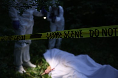 Photo of Forensic experts working at crime scene with dead body outdoors, focus on yellow police tape