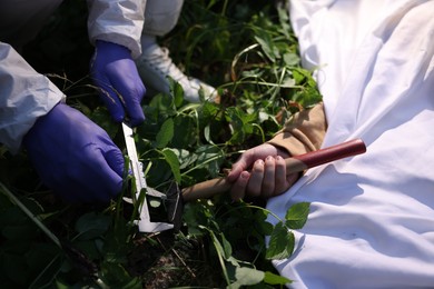 Photo of Forensic expert working at crime scene with dead body outdoors, closeup