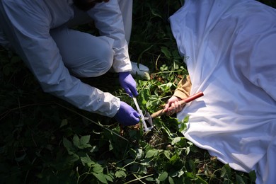 Photo of Forensic expert working at crime scene with dead body outdoors, closeup