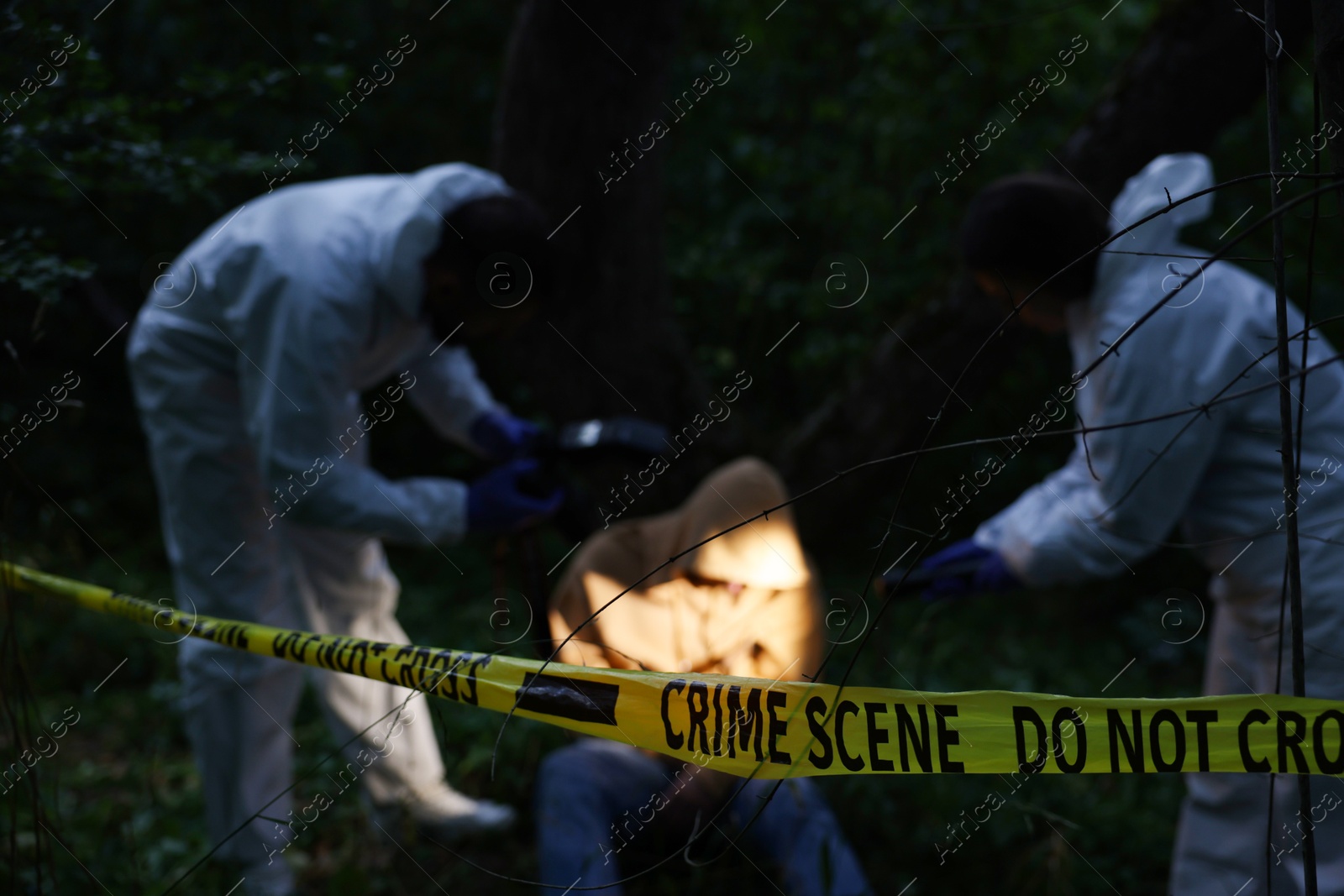 Forensic experts working at crime scene with dead body outdoors, focus on yellow police tape Photo of Forensic experts working at crime scene with dead body outdoors, focus on yellow police tape