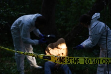 Photo of Forensic experts working at crime scene with dead body outdoors, focus on yellow police tape