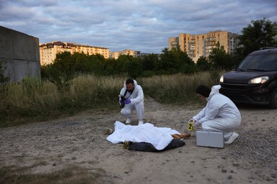Photo of Forensic experts working at crime scene with dead body outdoors, space for text