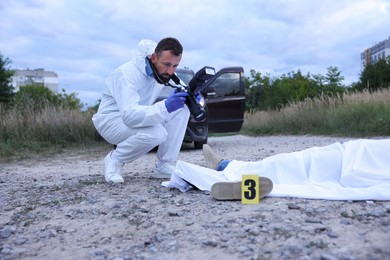 Photo of Forensic expert working at crime scene with dead body outdoors