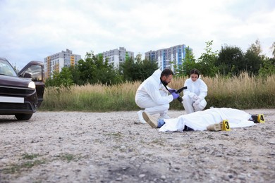 Photo of Forensic experts working at crime scene with dead body outdoors, space for text