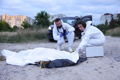 Photo of Forensic experts working at crime scene with dead body outdoors