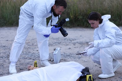 Photo of Forensic experts working at crime scene with dead body outdoors