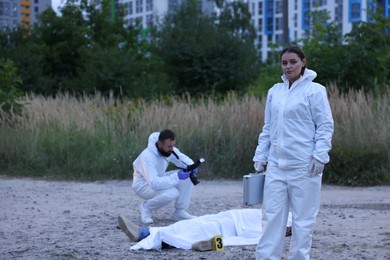 Photo of Forensic experts working at crime scene with dead body outdoors