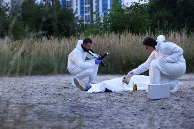 Photo of Forensic experts working at crime scene with dead body outdoors