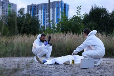 Photo of Forensic experts working at crime scene with dead body outdoors