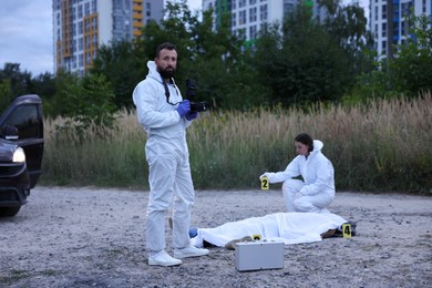 Photo of Forensic experts working at crime scene with dead body outdoors