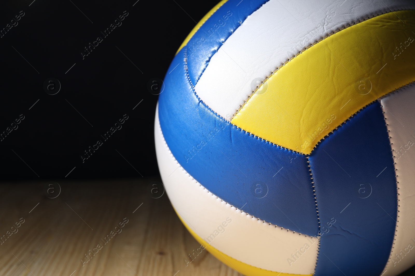 Photo of One volleyball ball on wooden surface against black background, closeup. Space for text