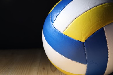 Photo of One volleyball ball on wooden surface against black background, closeup. Space for text