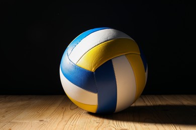 Photo of One volleyball ball on wooden surface against black background