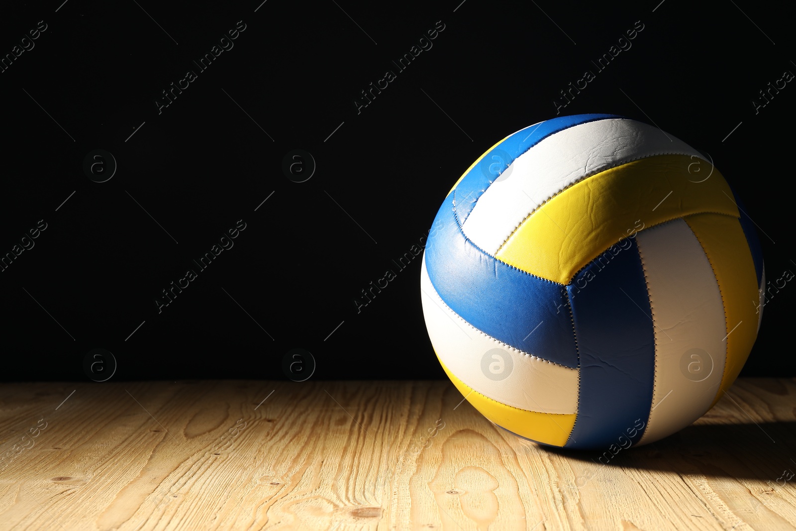 Photo of One volleyball ball on wooden surface against black background, space for text