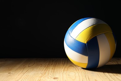 Photo of One volleyball ball on wooden surface against black background, space for text