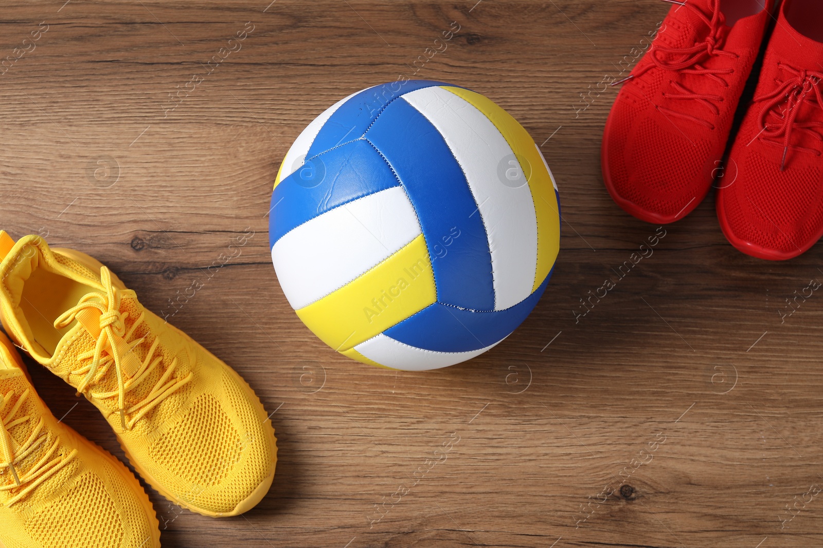 Photo of Volleyball ball and sneakers on wooden surface, flat lay