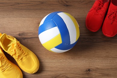 Photo of Volleyball ball and sneakers on wooden surface, flat lay