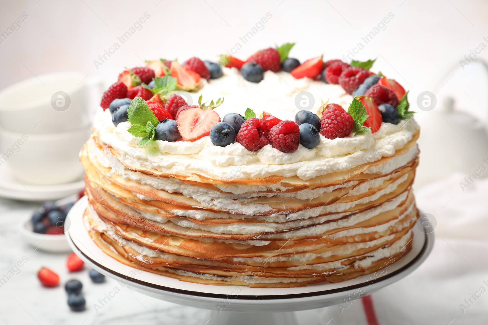 Photo of Delicious crepe cake with fresh berries on white table, closeup
