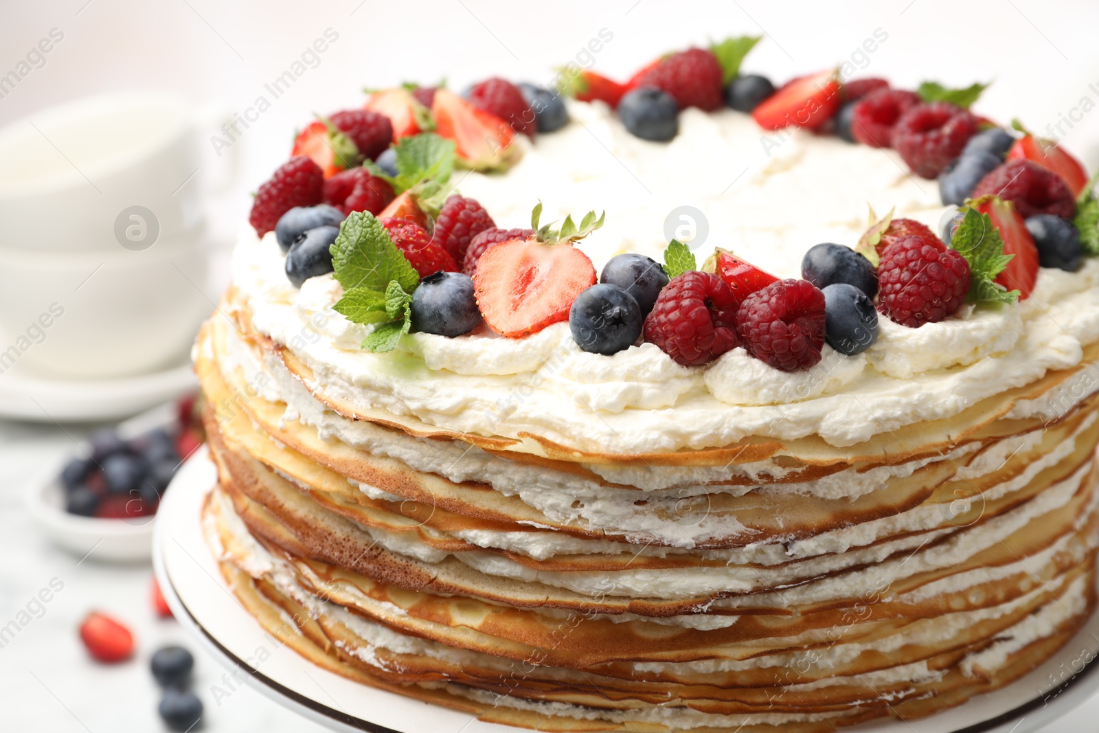 Photo of Delicious crepe cake with fresh berries on white table, closeup