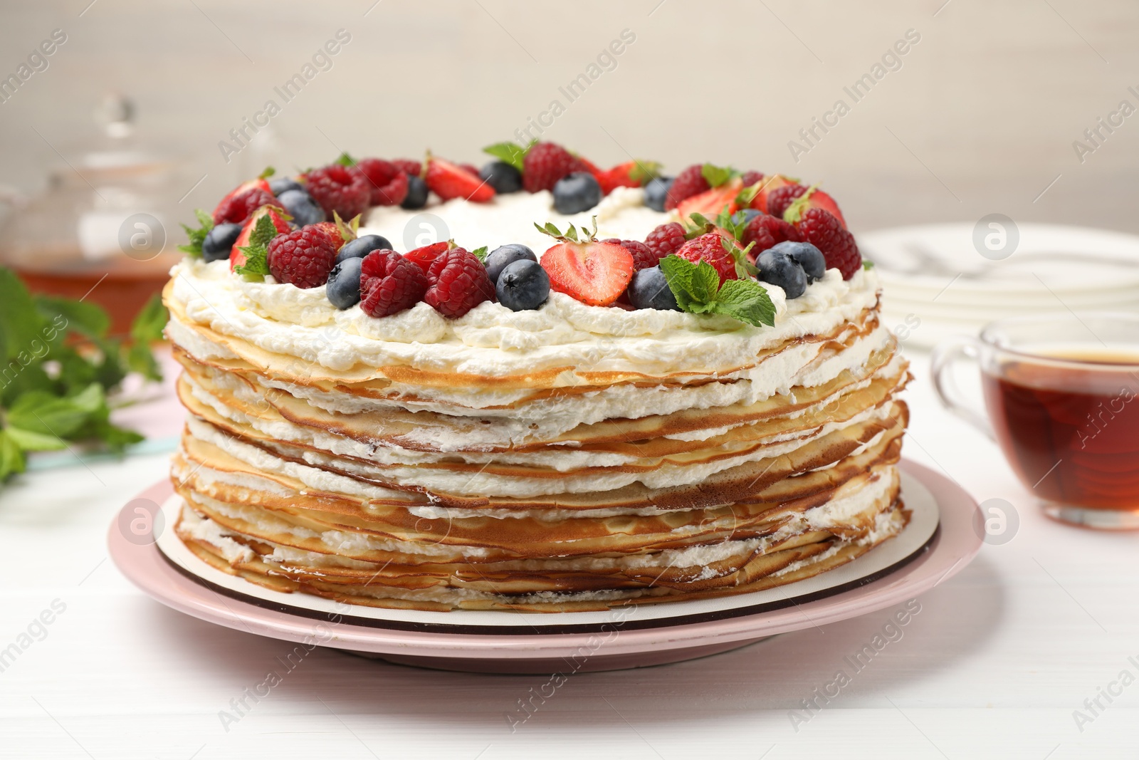 Photo of Delicious crepe cake with fresh berries and tea on white wooden table, closeup