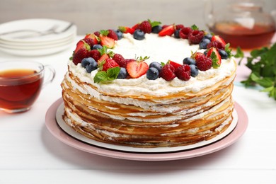 Photo of Delicious crepe cake with fresh berries and tea on white wooden table, closeup