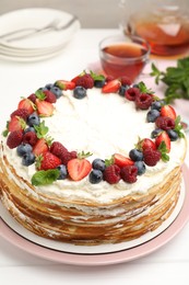 Photo of Delicious crepe cake with fresh berries and tea on white wooden table, closeup