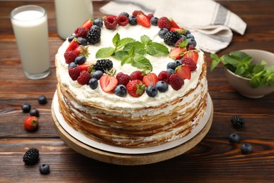 Photo of Delicious crepe cake with fresh berries and milk on wooden table, closeup