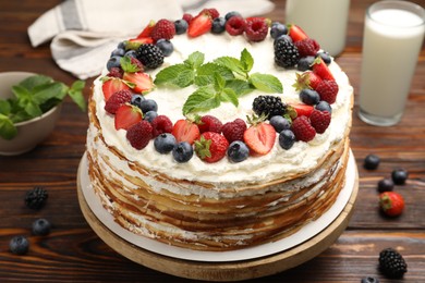 Photo of Delicious crepe cake with fresh berries and milk on wooden table, closeup