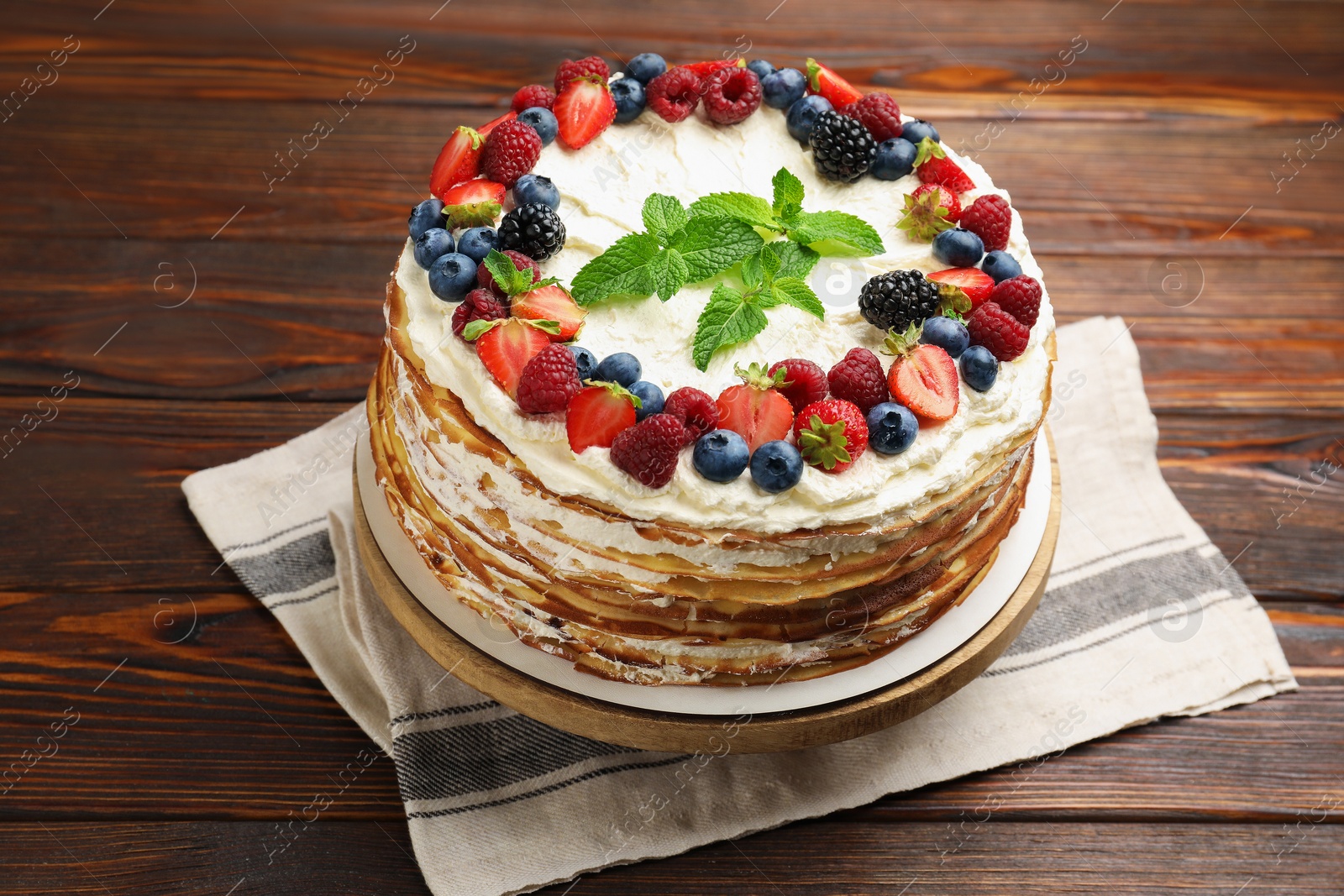 Photo of Delicious crepe cake with fresh berries on wooden table