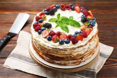 Photo of Delicious crepe cake with fresh berries and server on wooden table, closeup