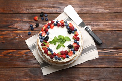 Photo of Delicious crepe cake with fresh berries and server on wooden table, top view