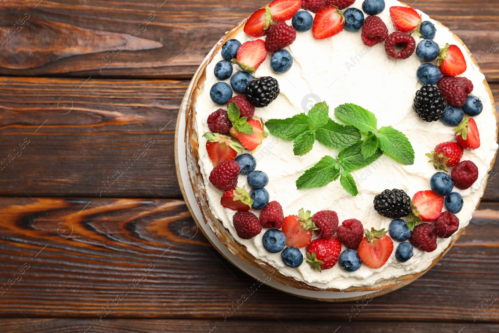 Photo of Delicious crepe cake with fresh berries on wooden table, top view. Space for text