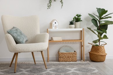Photo of Stylish armchair, console table and houseplants in room. Interior design