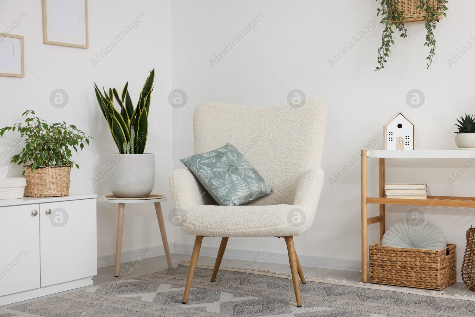 Photo of Stylish armchair, cabinet, console table and houseplants in room. Interior design