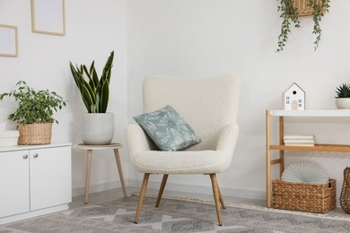 Photo of Stylish armchair, cabinet, console table and houseplants in room. Interior design