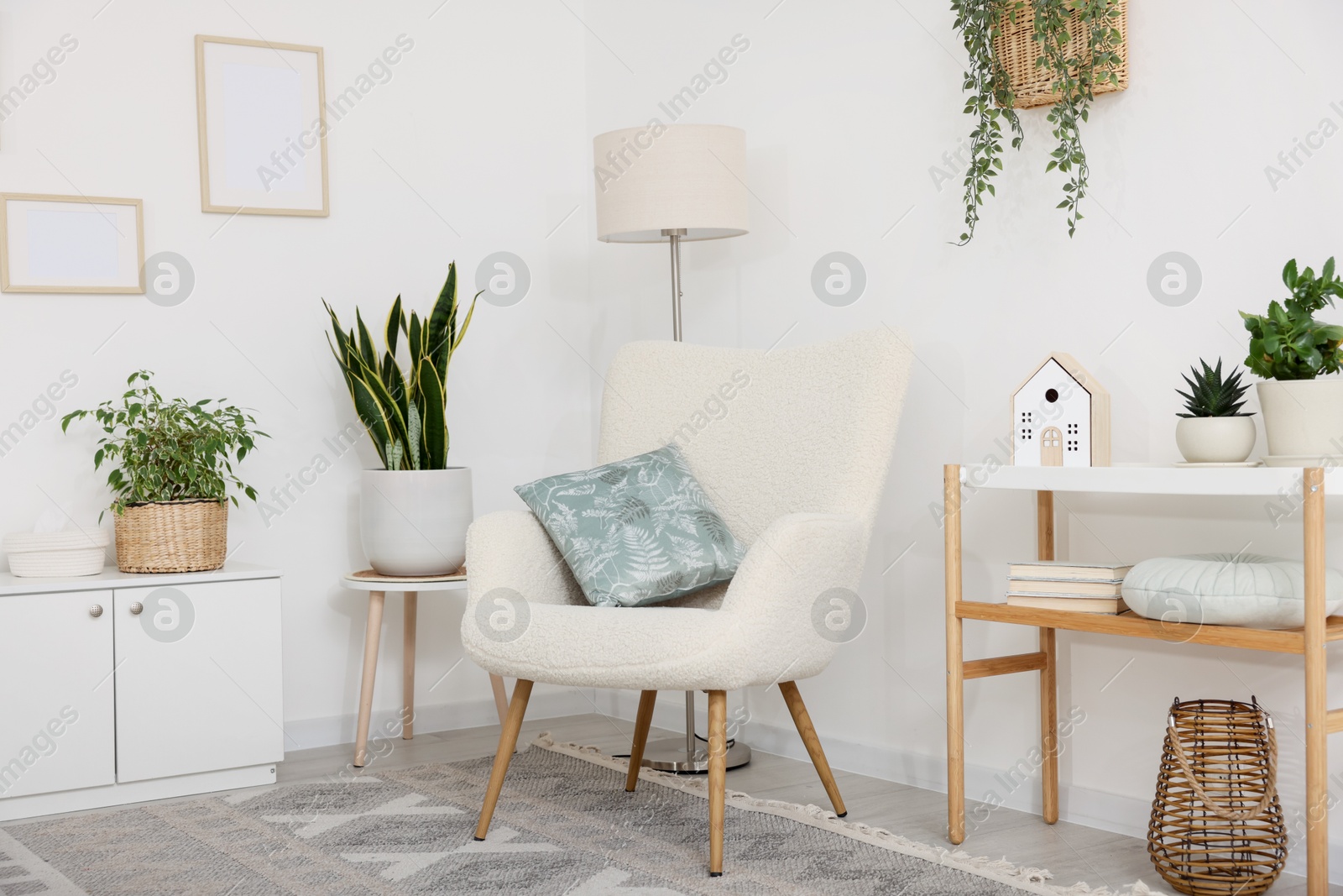 Stylish armchair, lamp, cabinet, console table and houseplants in room. Interior design Photo of Stylish armchair, lamp, cabinet, console table and houseplants in room. Interior design
