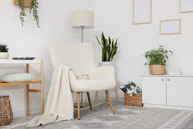 Photo of Stylish armchair, lamp, cabinet, console table and houseplants in room. Interior design