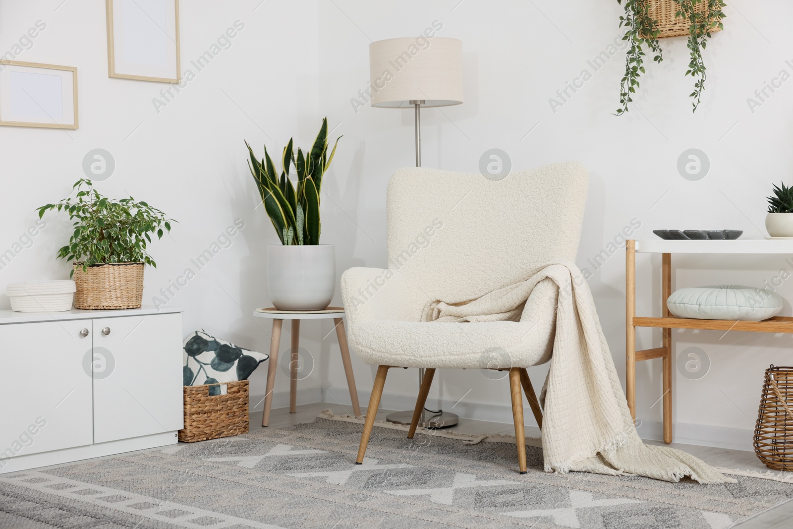 Stylish armchair, lamp, cabinet, console table and houseplants in room. Interior design Photo of Stylish armchair, lamp, cabinet, console table and houseplants in room. Interior design