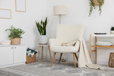 Photo of Stylish armchair, lamp, cabinet, console table and houseplants in room. Interior design