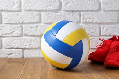 Photo of Volleyball ball and red sneakers on wooden surface against white brick wall