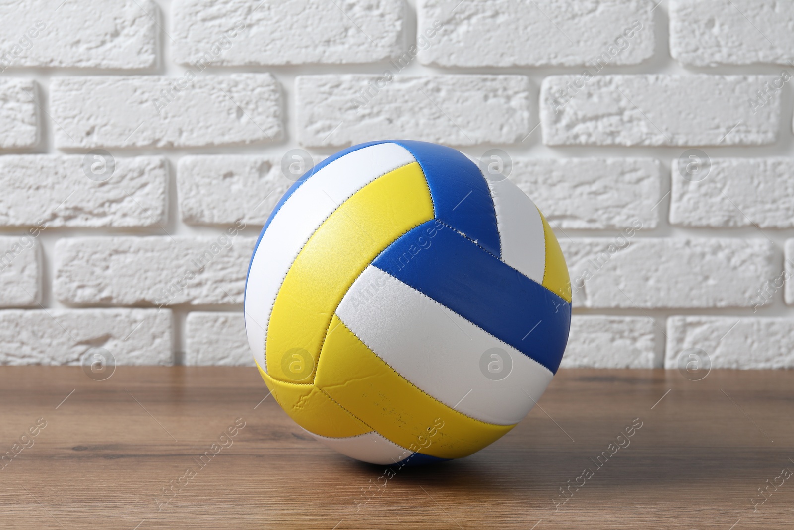 Photo of One volleyball ball on wooden surface against white brick wall
