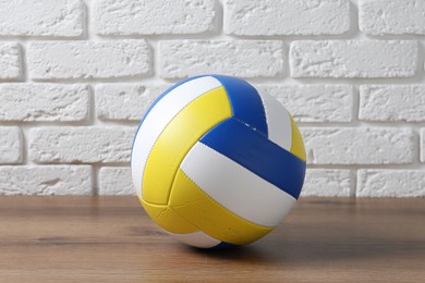 Photo of One volleyball ball on wooden surface against white brick wall