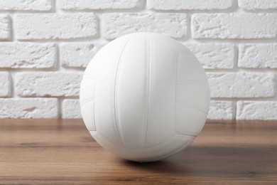 Photo of One volleyball ball on wooden surface against white brick wall
