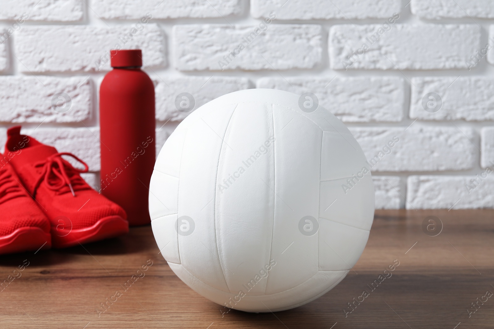 Photo of Volleyball ball, sneakers and water bottle on wooden surface against white brick wall, closeup
