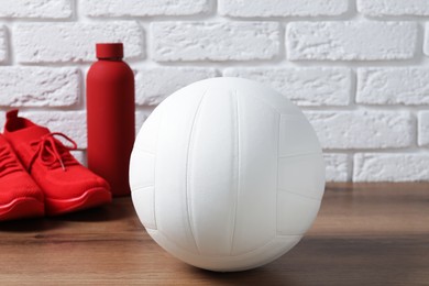 Photo of Volleyball ball, sneakers and water bottle on wooden surface against white brick wall, closeup