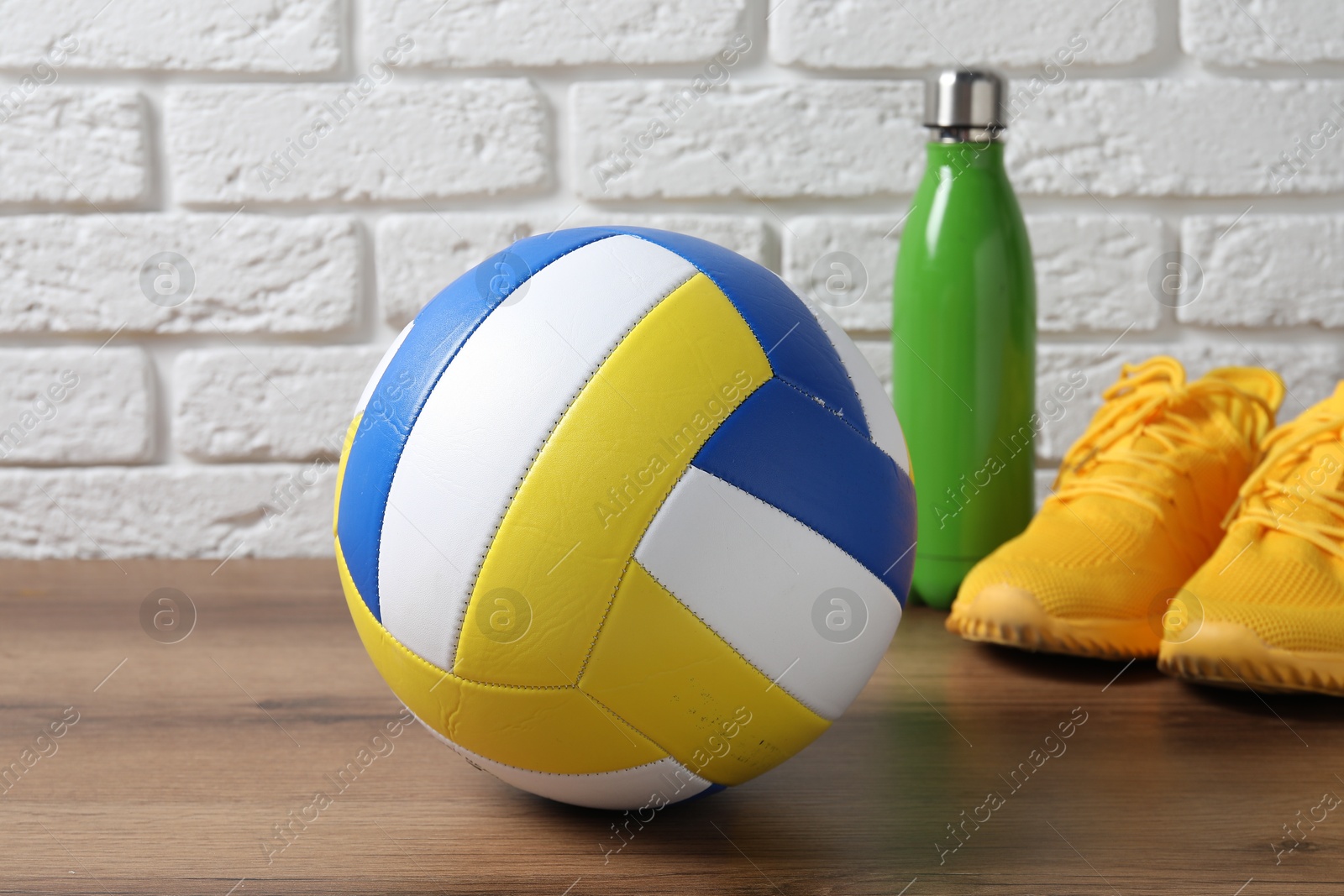 Photo of Volleyball ball, sneakers and water bottle on wooden surface against white brick wall, closeup
