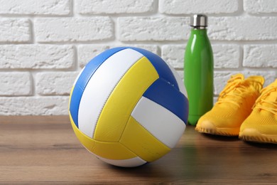 Photo of Volleyball ball, sneakers and water bottle on wooden surface against white brick wall, closeup
