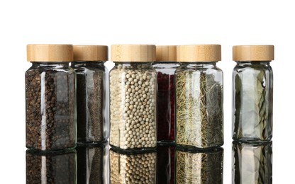 Photo of Many different aromatic spices in jars on mirror surface against white background