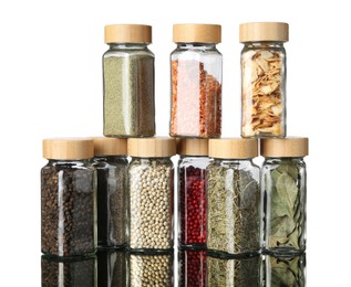 Photo of Many different aromatic spices in jars on mirror surface against white background