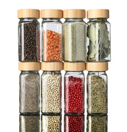Photo of Many different aromatic spices in jars on mirror surface against white background